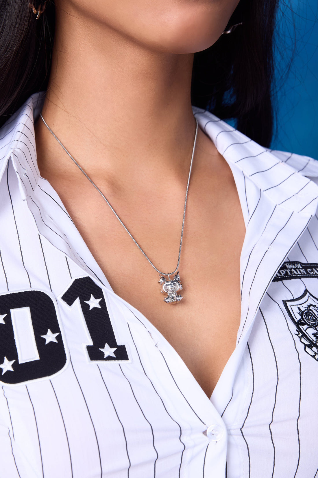 EFE Dog Drop Necklace on model — silver snake chain with gold-plated FEFE dog figure pendant, worn solo at chest level with white pinstripe baseball shirt