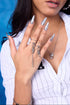 Riot Spike Ring Set on model — silver stacking rings with ball chain drop and spike pendant on middle finger, layered with slim band rings, chrome stiletto nails, FEFE Dog Necklace visible at chest, blue backdrop